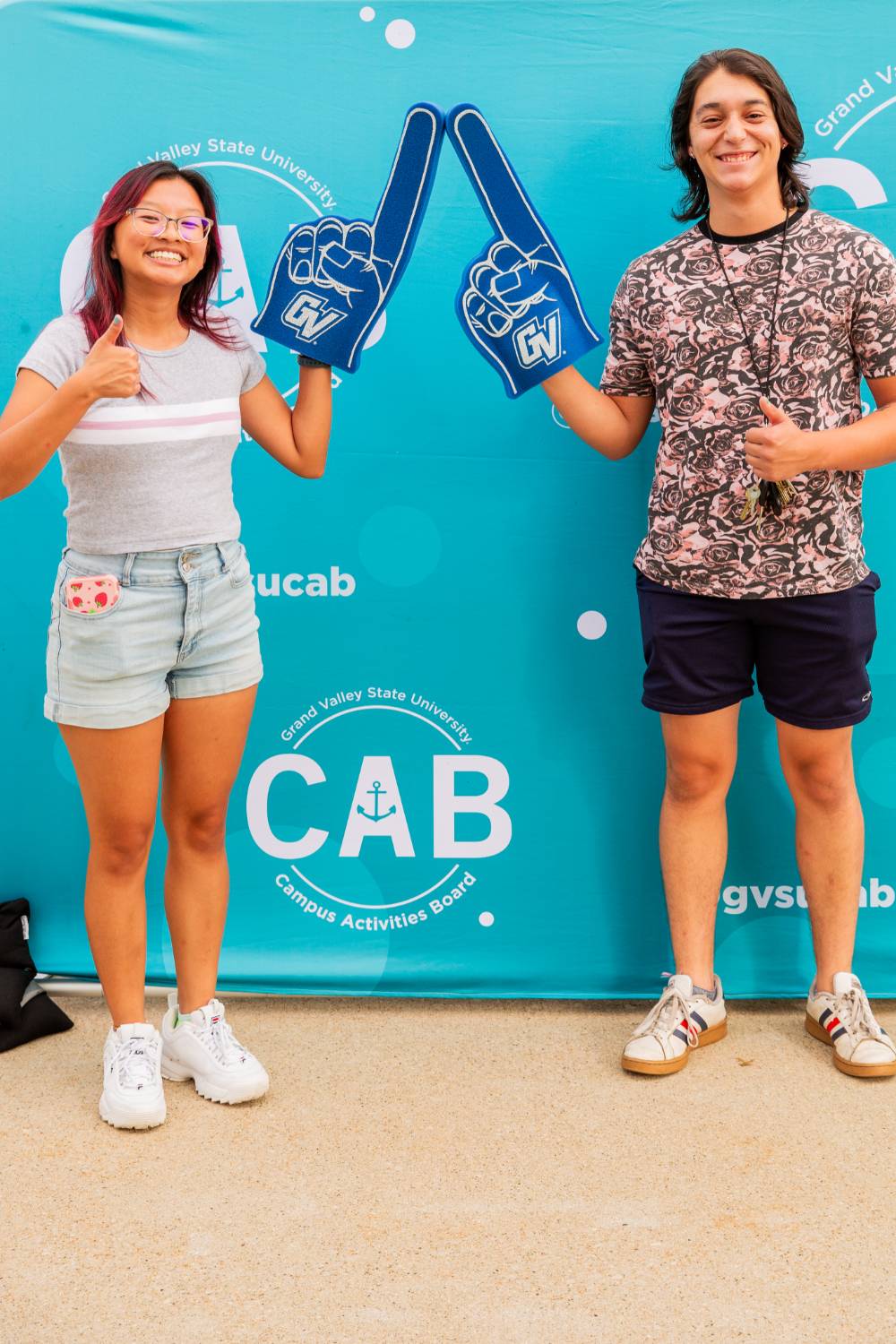 students holding foam fingers and posing in front of CAB backdrop at Laker Kickoff photo booth